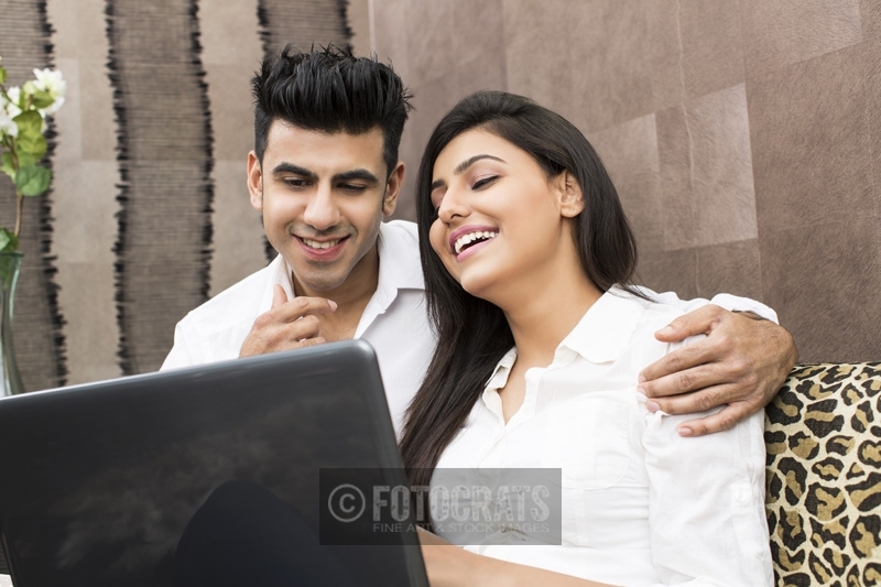 young couple laughing while browsing in laptop