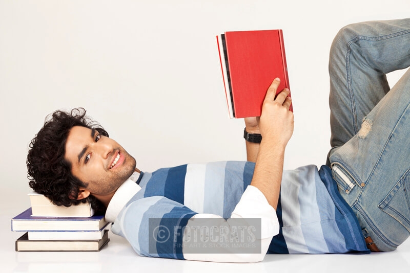 college boy lying down on pile of books 