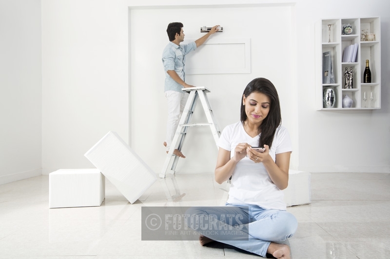 husband decorating home while wife messaging on mobile