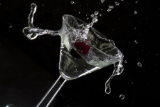 red cherry splashing into cocktail against black background