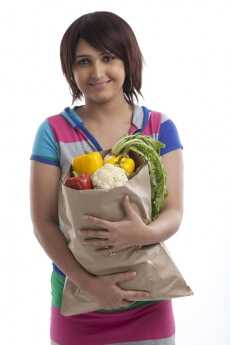 young housewife holding bag full of vegetables with both hands 