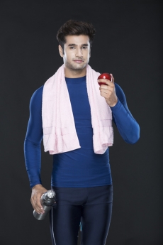 healthy young guy in gym wear holding an apple and sipper 