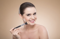 girl applying make up with brush while smiling