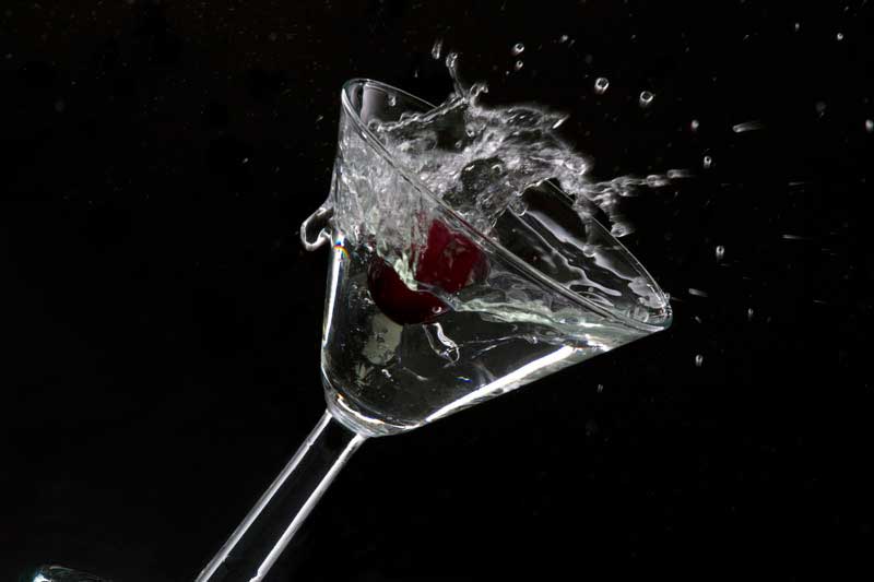 red cherry splashing into cocktail against black background
