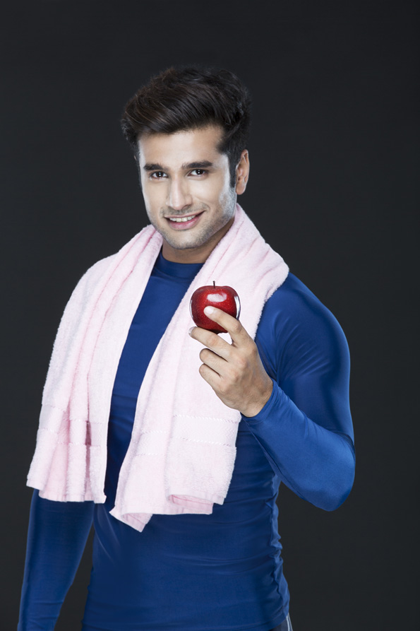man in gym wear holding fresh red apple and posing  